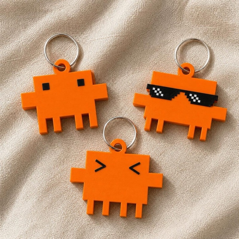 Three orange pixelated character keychains with silver metal rings.